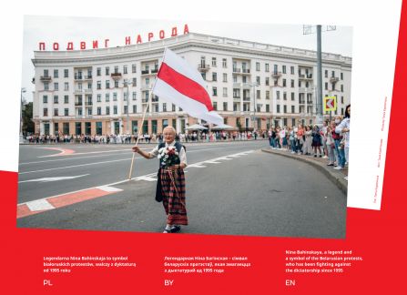 Photograph from the exhibition Belarus. road to freedom. an elderly woman with a historical Belarusian flag in the middle of the intersection. on the sidewalk next to a crowd of people, high tenement houses in the background.